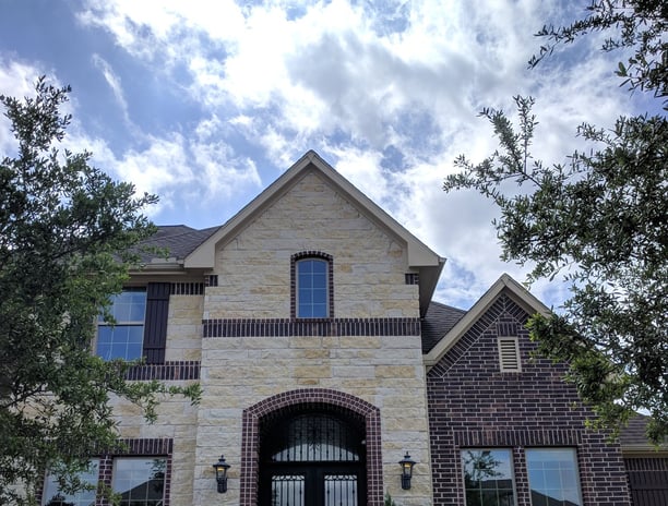 A beige stone and red brick two story home sparkling and spotless after receiving window cleaning