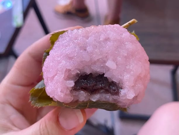 a person holding a pink sakura mochi with a anko inside