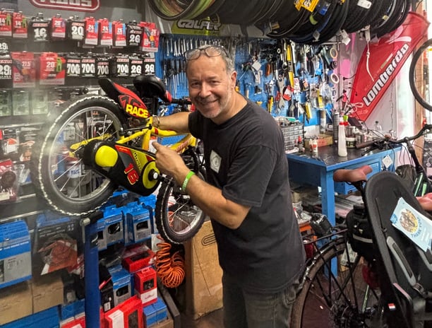 Federico, il proprietario di abicicomeprima, sorride intento ad aggiustare una bici da bambino
