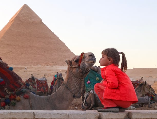 Petite fille fait un bisous au chameau devant les pyramides de Gizeh