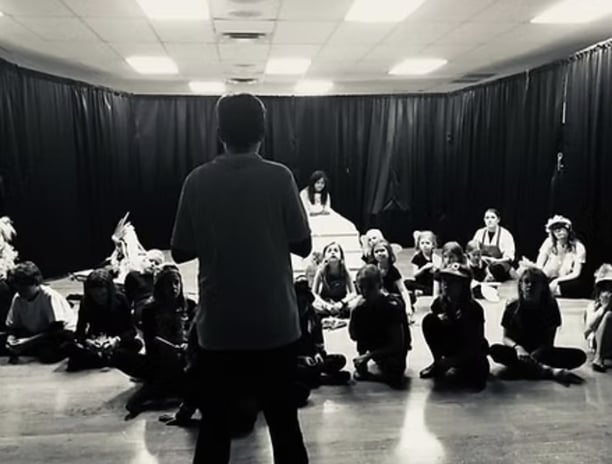 a youth director standing in front of a group of actors getting notes before the show.