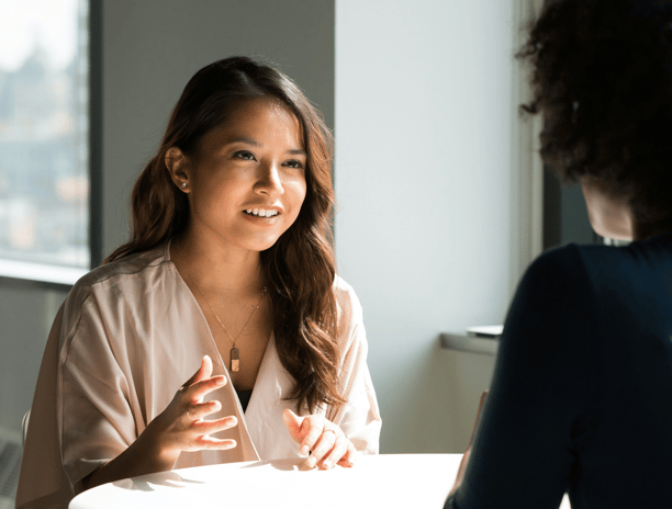 two women of color sitting at a table talking to each other