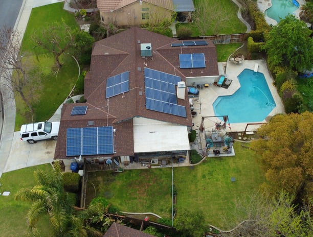 Aerial view of a house with solar panels on the roof and a pool in the backyard, showcasing a modern