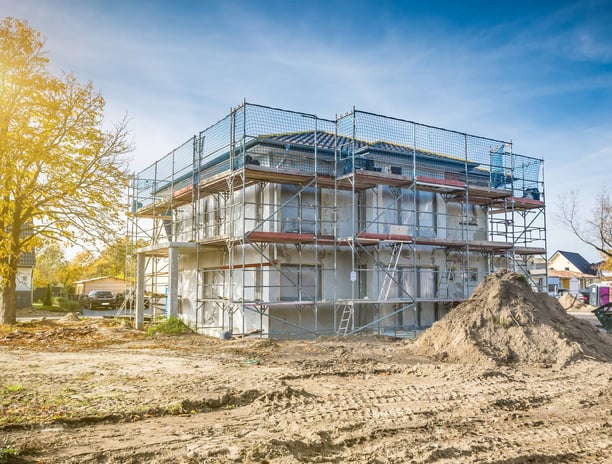 Eingerüstetes Gebäude während der Sanierungsarbeiten mit Baumaterial und Erdarbeiten im Vordergrund