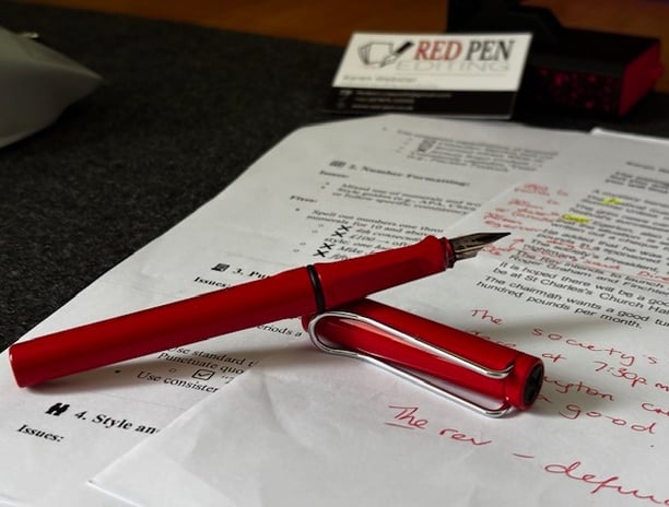 Red Lamy "Safari" fountain pen resting on manuscript that has been annotated by Red Pen Editing