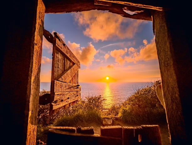 Cornish sunrise over the sea as seen though the open door of at hut at the top of a cliff