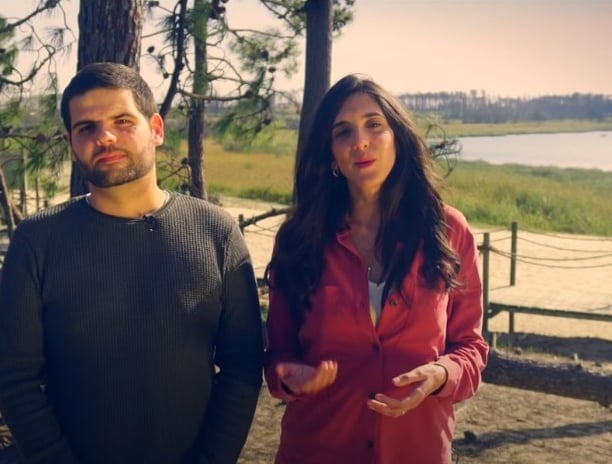 a man and woman standing in front of a lake