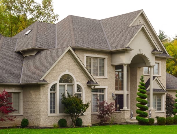 A stately tan brick house with beautiful landscaping and shrubery