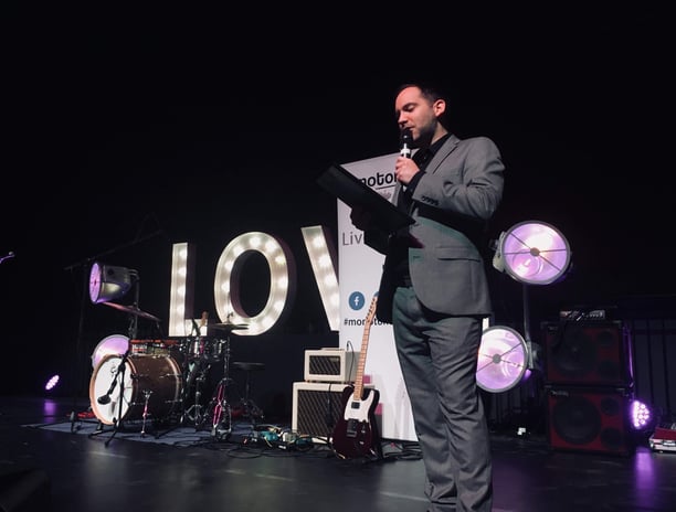 Alex hosting an awards event in front of giant letters spelling LOVE
