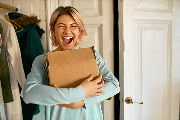 Mulher feliz e sorridente segurando uma caixa, parecendo ser um produto recém-entregue.