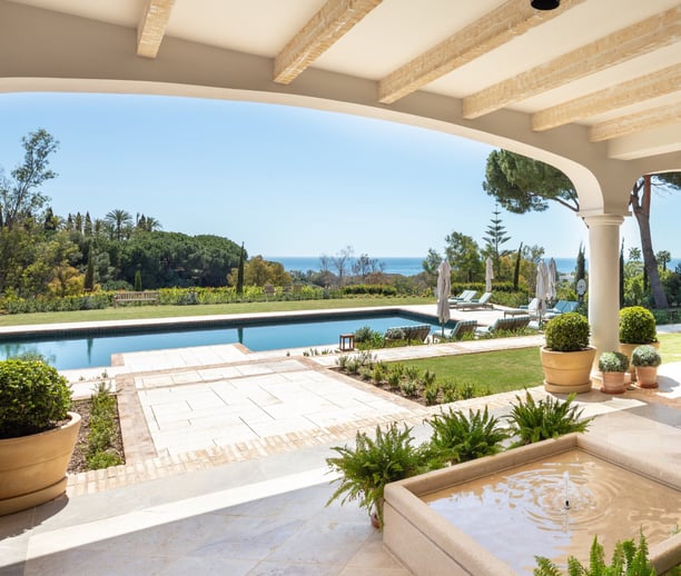 View from the shaded porch across the pool, with the Mediterranean Sea visible in the background.