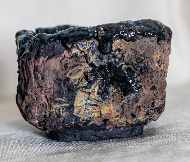 Raku-fired Kurinuki cup from Amman, Jordan, with black glaze, ochre tones, and volcanic textures