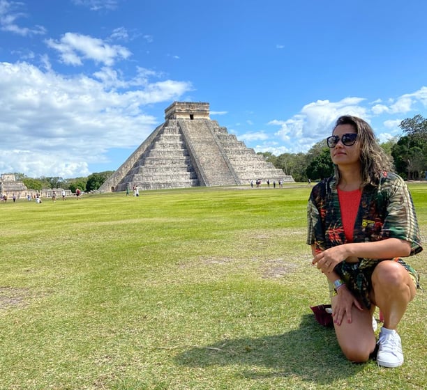 mulher de joelho em frente a pirâmide Chichén Itzá no méxico
