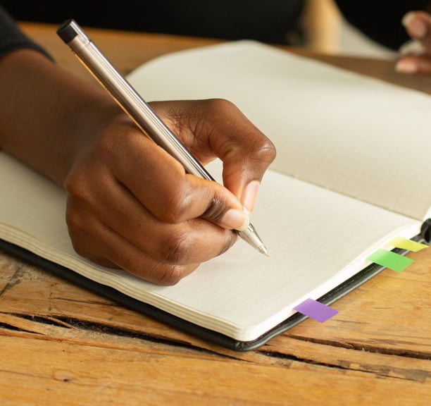 a person holding a pen and writing on a notebook