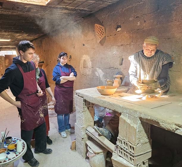 Un artisan devant un tour de poterie en train de créer une coupe en argile