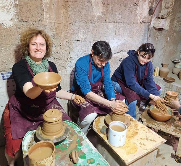 Une femme est assise devant un tour de poterie en train de montre une coupe en argile