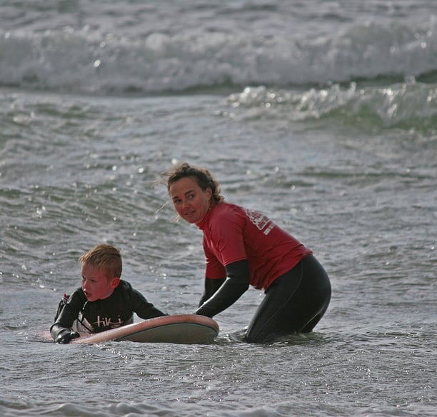 A young surfer with a female surf coach holding the board waiting for a wave