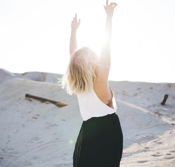 Une femme debout dans le sable, les bras levés, symbole de liberté et de bien-être