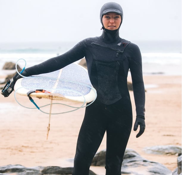 A female surfer in full winter wetsuit equipment holding a longbaord