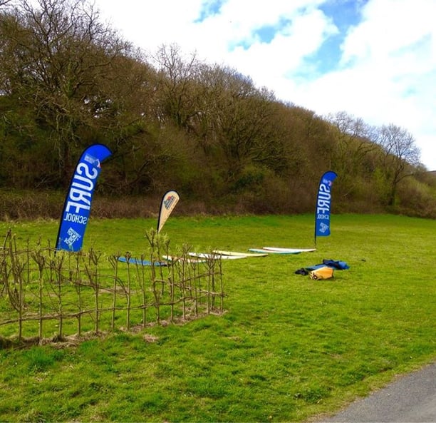 Surfboards laid on grass with surf school teardop flags