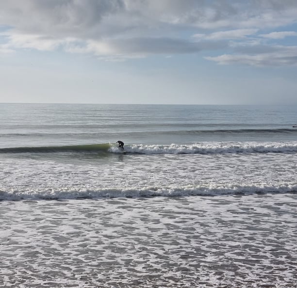 A surfer trimming along a clean peeling wave at Ynyslas, calm seas and blue skies.