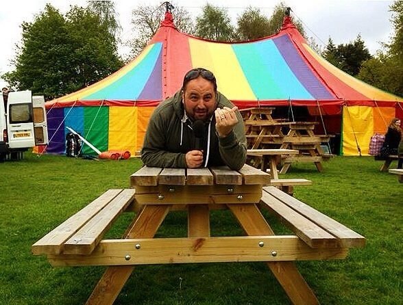 Wynne Evans lying on a picnic beach with a colourful circus tent in the background