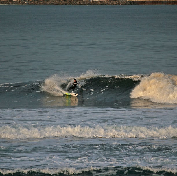 surfer performing a forehand cutback with the early mornig sun catching the wave