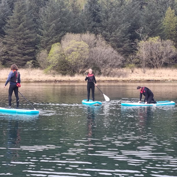 2 paddle board students and SUP coach on a calm lake.