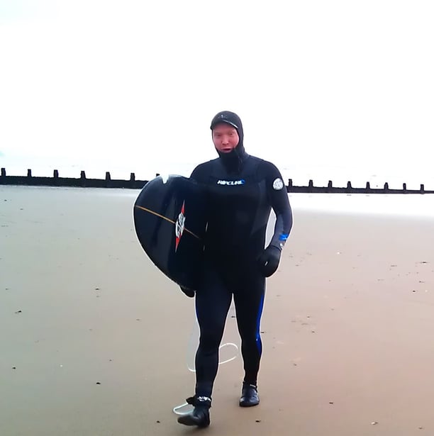 A male surfer walking up Ynyslas beach in full winter setsuit gear