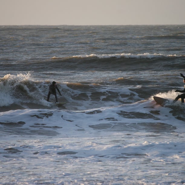 Two surfers riding towards each other in wintery sunshine