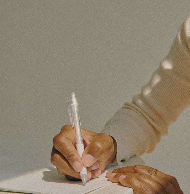 Mano di donna con pelle scura che scrive su un quaderno bianco con una penna trasparente