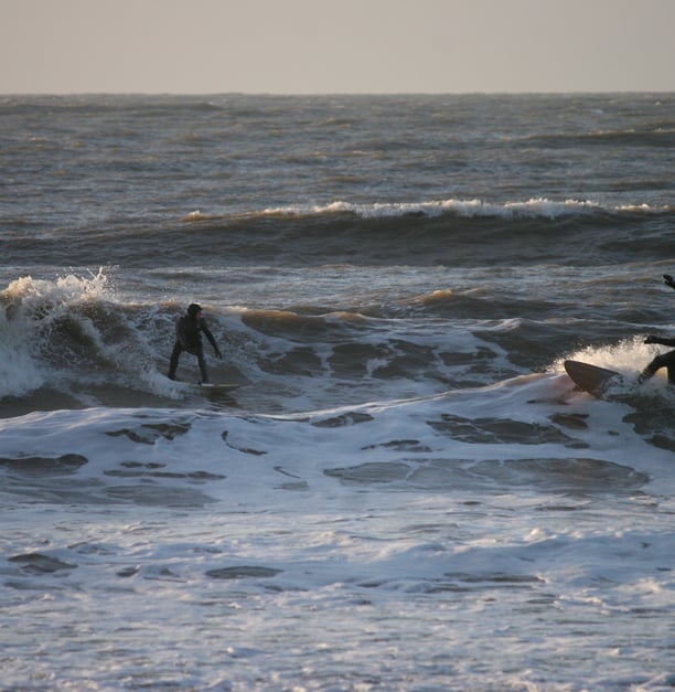 Two surfers riding towards each other in wintery sunshine