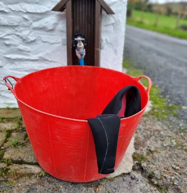 A wetsuit in a red bucket about to be rinsed