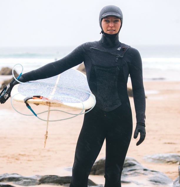 A female surfer in full winter wetsuit equipment holding a longbaord