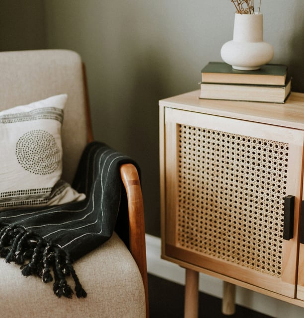 Un fauteil avec un plaid, à côté un vase et des livres posés sur un meuble en bois
