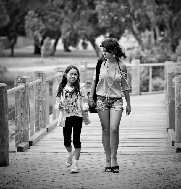 Girl and child strolling over a wooden bridge, deep in conversation