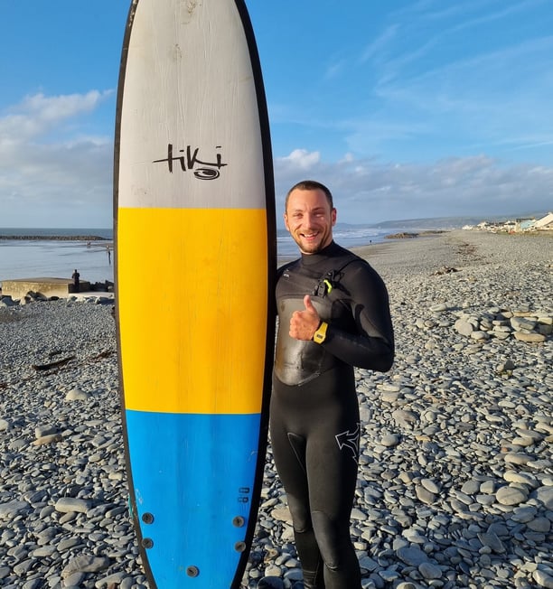 Surf coach Matt, holding a Tiki Grizzly surf board and giving the thumbs up