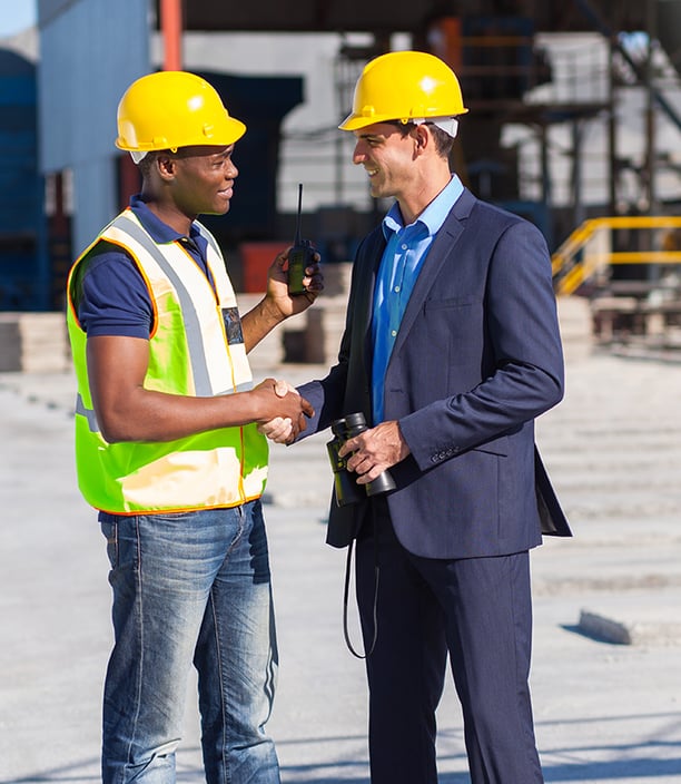 Photo of male supervisor in yellow hard hat shakes the hand of male employee in yellow hard hat.