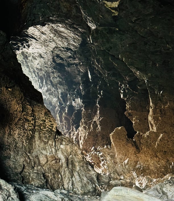 Photo of a huge cave with light at the end of the tunnel, Merlins cave Cornwall