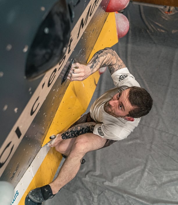 Grimpeur concentré sur un mur de bloc en salle, en pleine action sur une prise