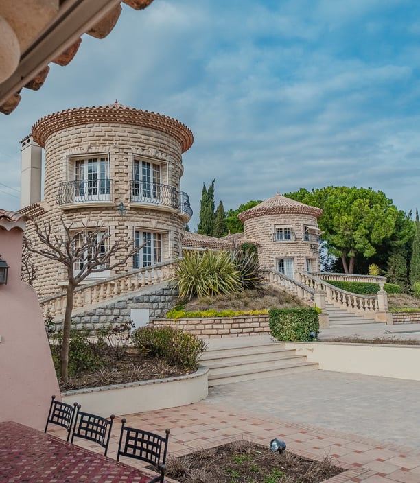 Villa de luxe en pierre avec tours, escalier élégant et jardin arboré