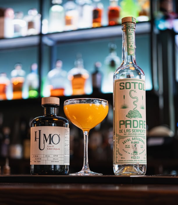 Cocktail mexicain à base de liqueur Humo au chipotle et Sotol Padre, sur fond de bar moderne