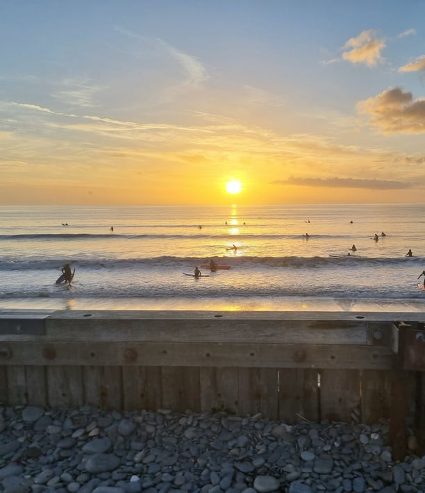 An amazing orange sun setting into the sea while. abusy after school club surf lesson goes on.