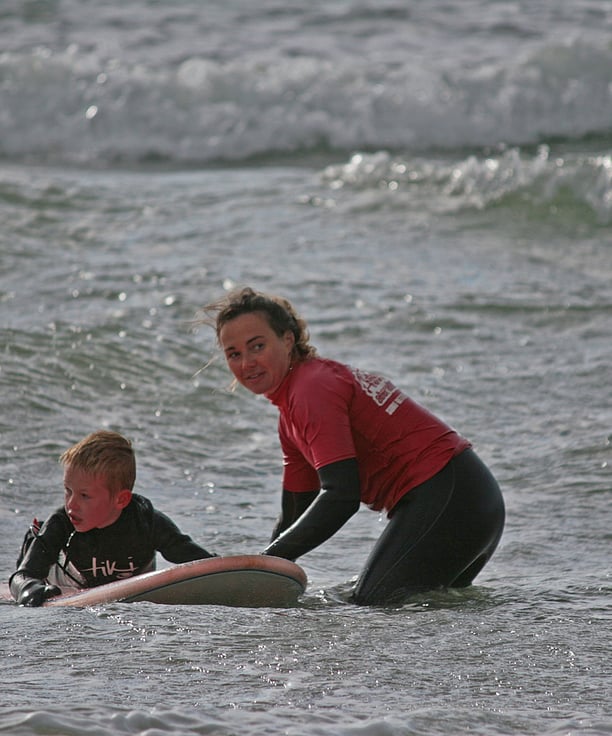 A young surfer with a female surf coach holding the board waiting for a wave