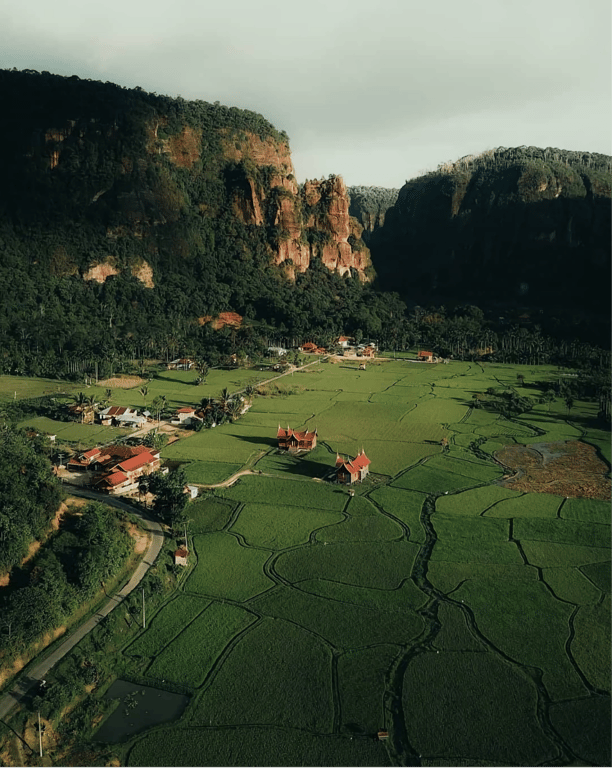 Scenic view of The Harau Valley with steep granite cliffs, lush green rice fields, and blue skies in West Sumatra, Indonesia.