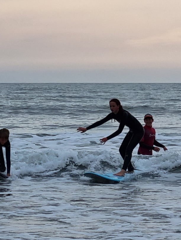After school surf club lesson witha young female surfer riding a wave on a baby blue surfboard