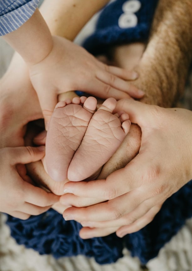 Mains de toutes la famille qui tiennent les pieds du nouveau-né