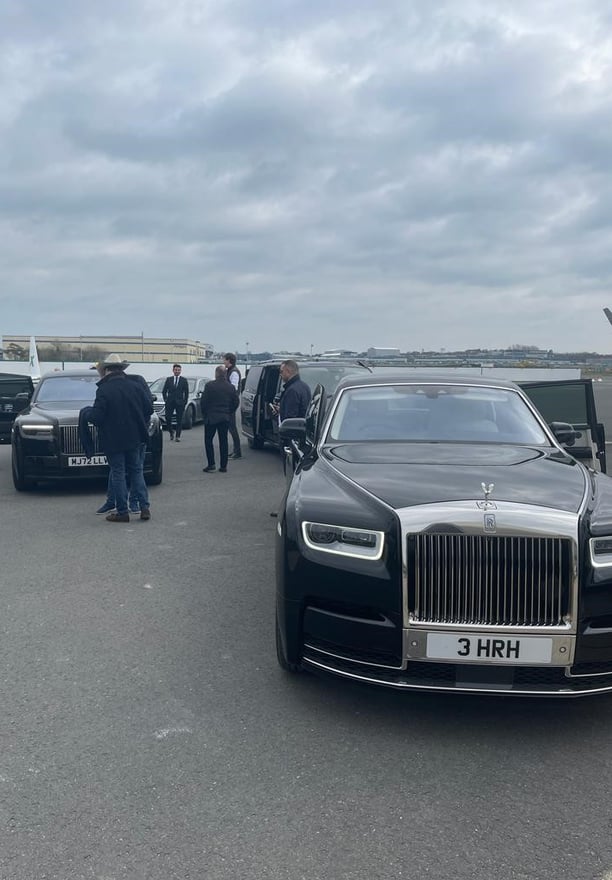 a rolls royce black car parked in front of a plane