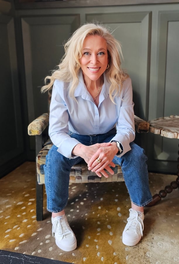 a blond woman sitting in a chair. she's wearing a blue button down shirt.