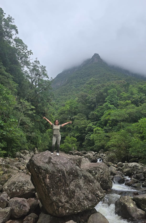 mulher com uma experiência incrível sobre uma pedra imensa na trilha do rio do boi em Praia Grande
